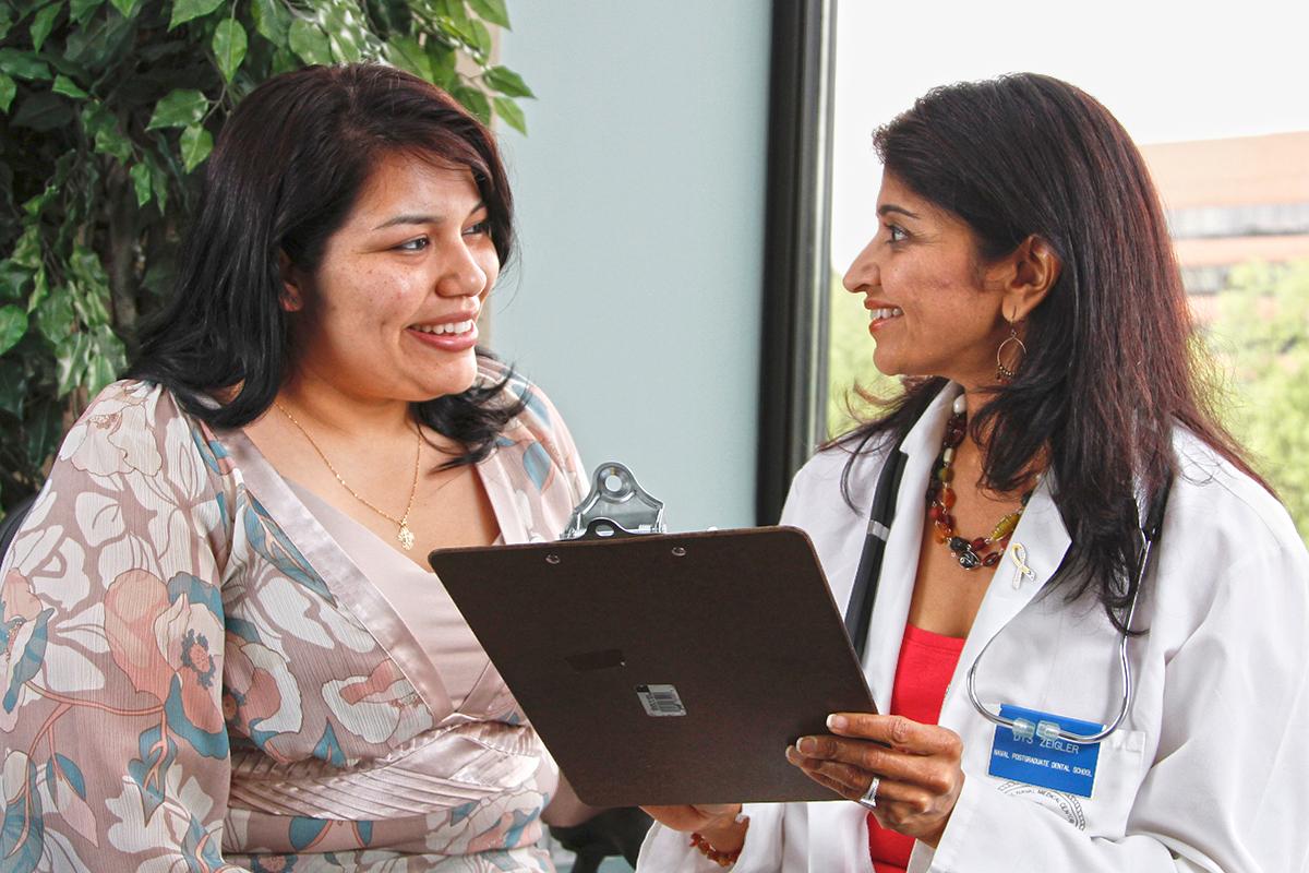 A woman doctor holding a clipboard talks with a woman patient.