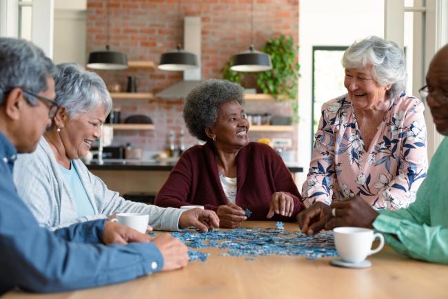 Diverse group of older people socializing while doing a puzzle.