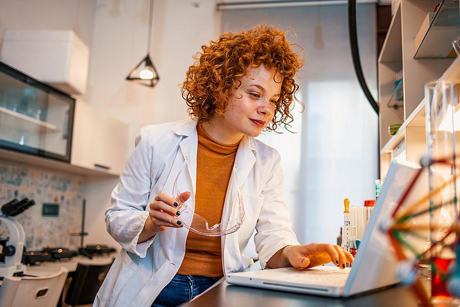 Biologist sitting at a lab table, looking at the laptop screen while studying test results.