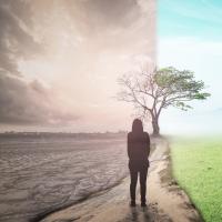 Woman standing on a road between a bleak, desolate area and a lush, green area.