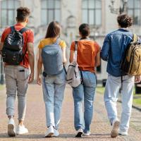 Five students with backpacks walking together on a campus pathway.