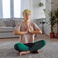 A woman wearing a headscarf practicing yoga in her living room.